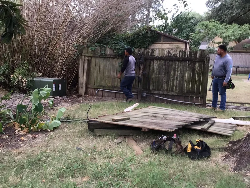 An old weathered grey fence being taken down, with removed panels stacked on the grass