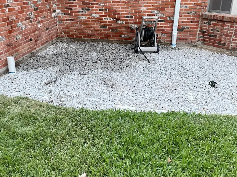 A bare side yard of loose white gravel and dirt in the corner of a brick house