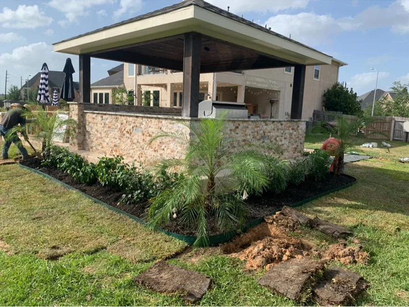 The same pavilion finished in stone veneer with new planting beds, palms and sod around it