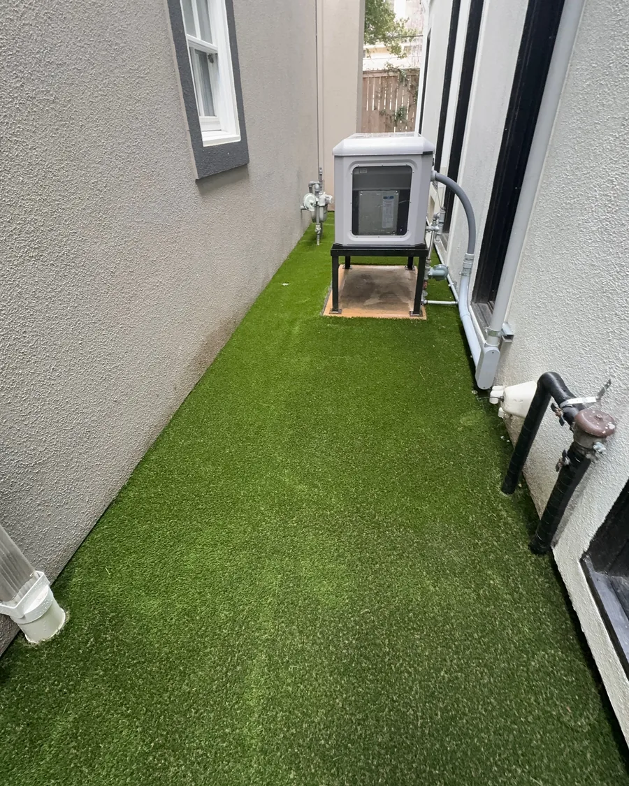 Artificial turf laid the length of a narrow side yard beside a stucco wall