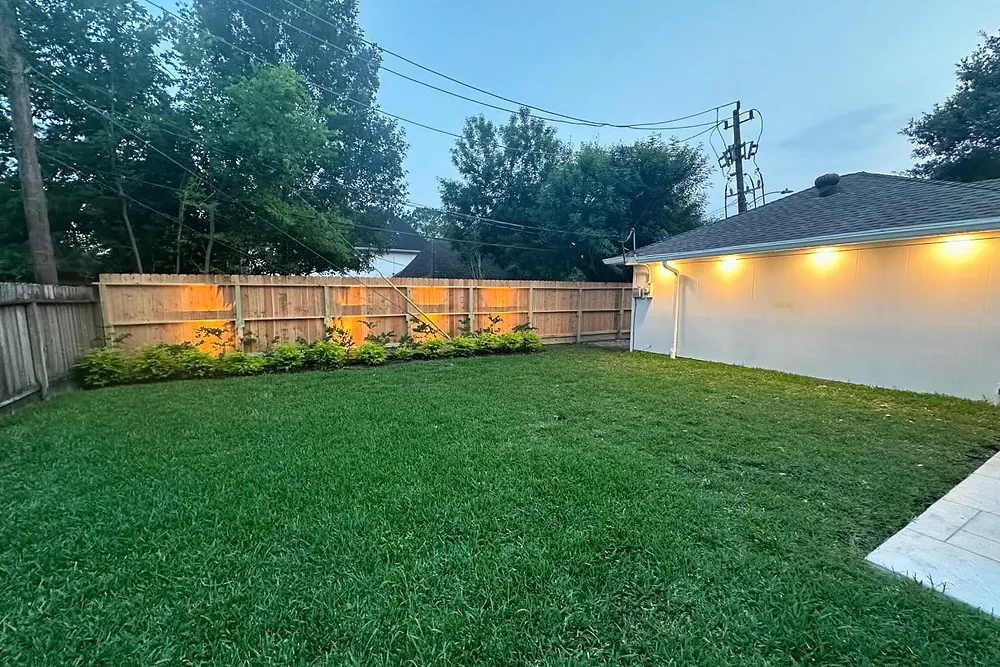 Backyard with warm landscape lighting along the house at dusk